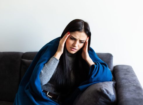 Indisposed woman feeling her temperature while resting on the sofa at home