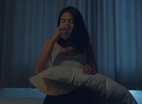 Beautiful Asian young woman sitting on bed take sleeping pill or night medicine in bedroom. Unhealthy sick Indian female suffers from insomnia or headache, depressed girl holds antidepressant meds.