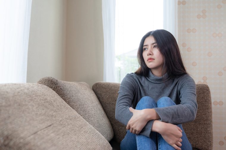 Unhappy asian pretty young woman siting alone on couch with feeling sadness